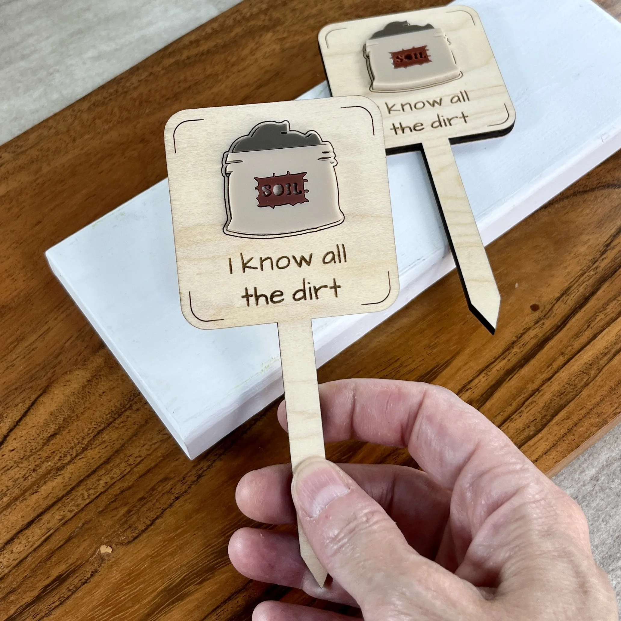 handheld maple plant stake featuring an acrylic bag of soil embellishment engraved with the phrase "I know all the dirt".