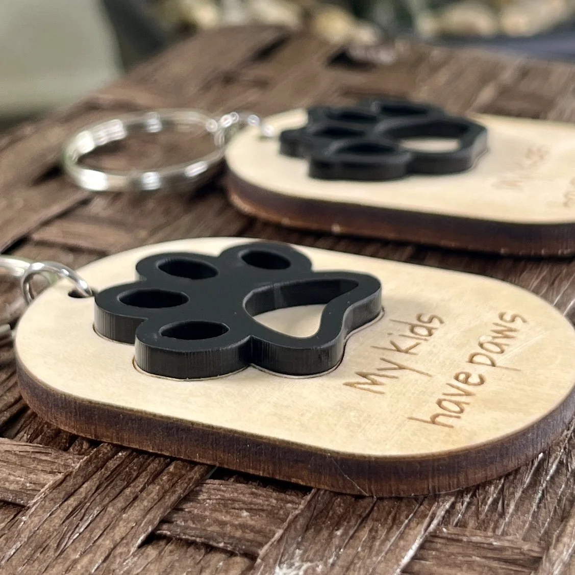 side view of laser cut maple wood keychain with raised matte black paw graphic to show depth and texture of product.