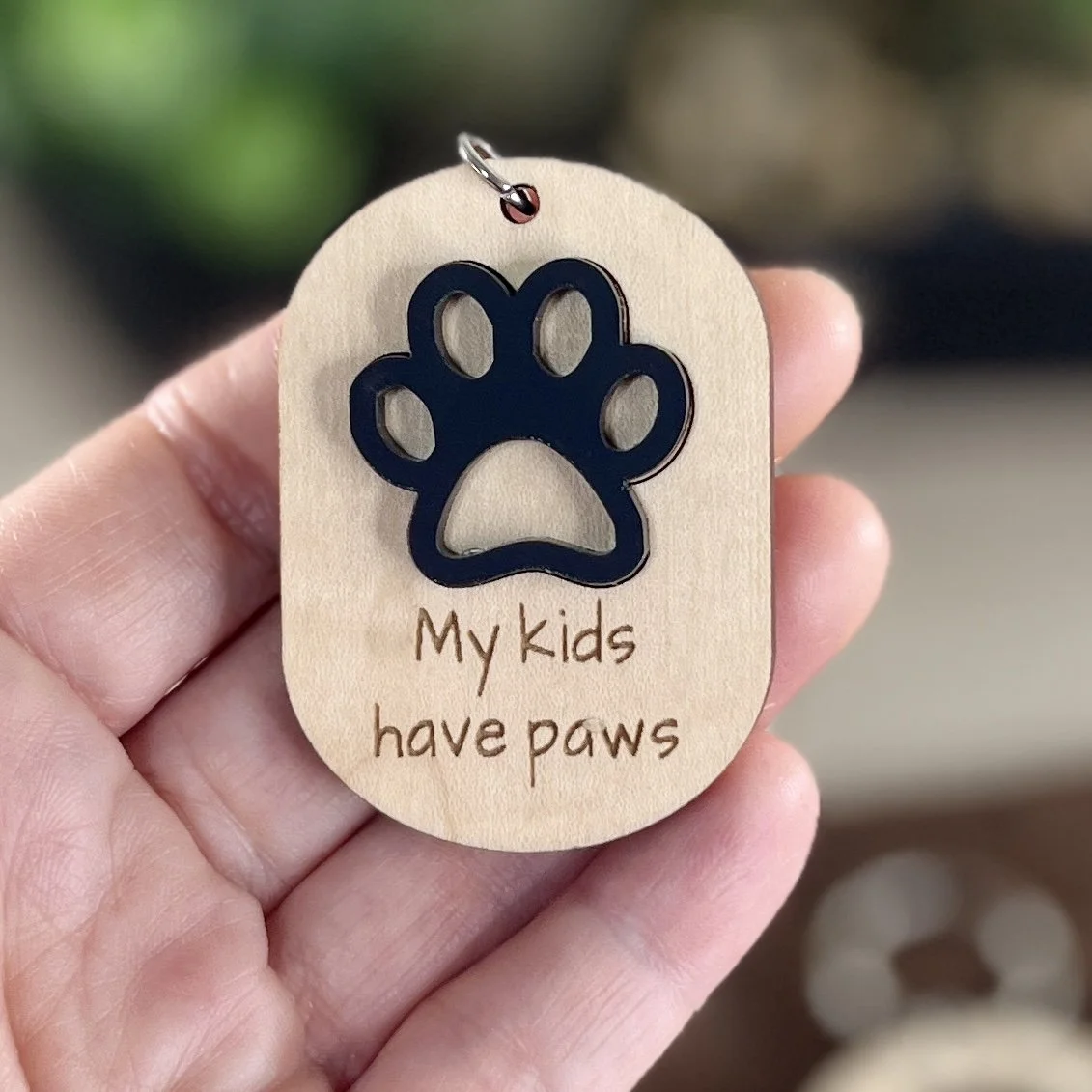 handheld shot of laser cut wood keychain with matte black paw and engraved saying "My kids have paws".