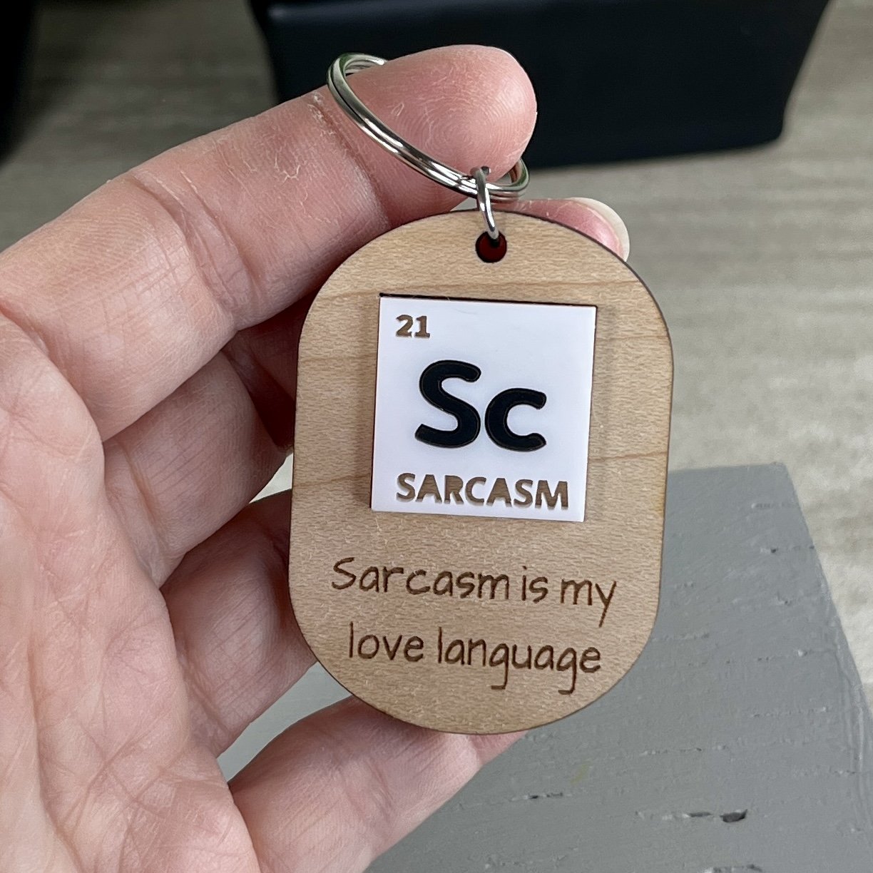 handheld laser cut maple wood keychain with a periodic table-inspired acrylic tile reading "Sc" for Sarcasm and the engraved phrase "Sarcasm is my love language".