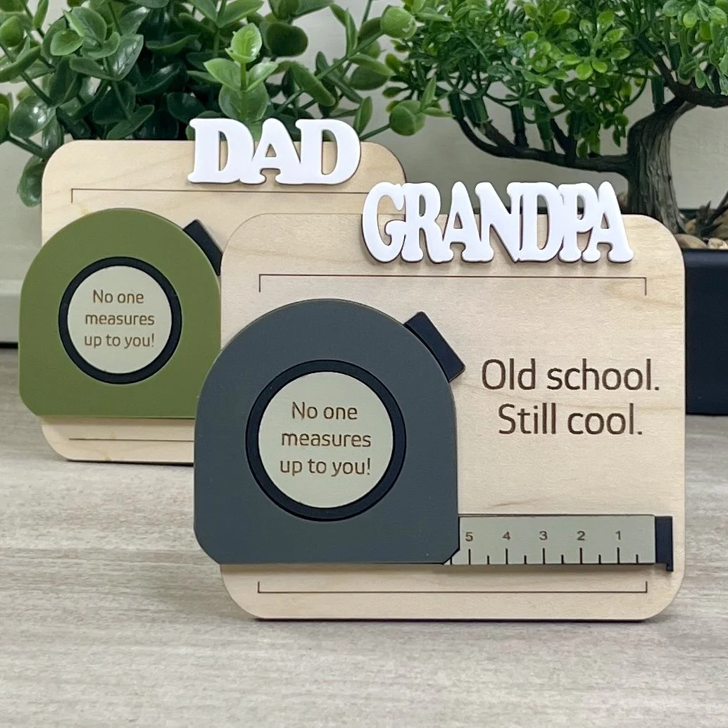 Set of maple wood magnets featuring 3D white headers for DAD and GRANDPA. Displays olive green and charcoal grey acrylic tape measure options on an engraved background.