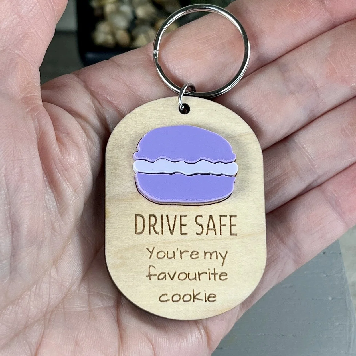 handheld laser cut maple wood keychain with macaron cookie in matte orchid/white acrylic and the engraved phrase "DRIVE SAFE You're my favourite cookie".