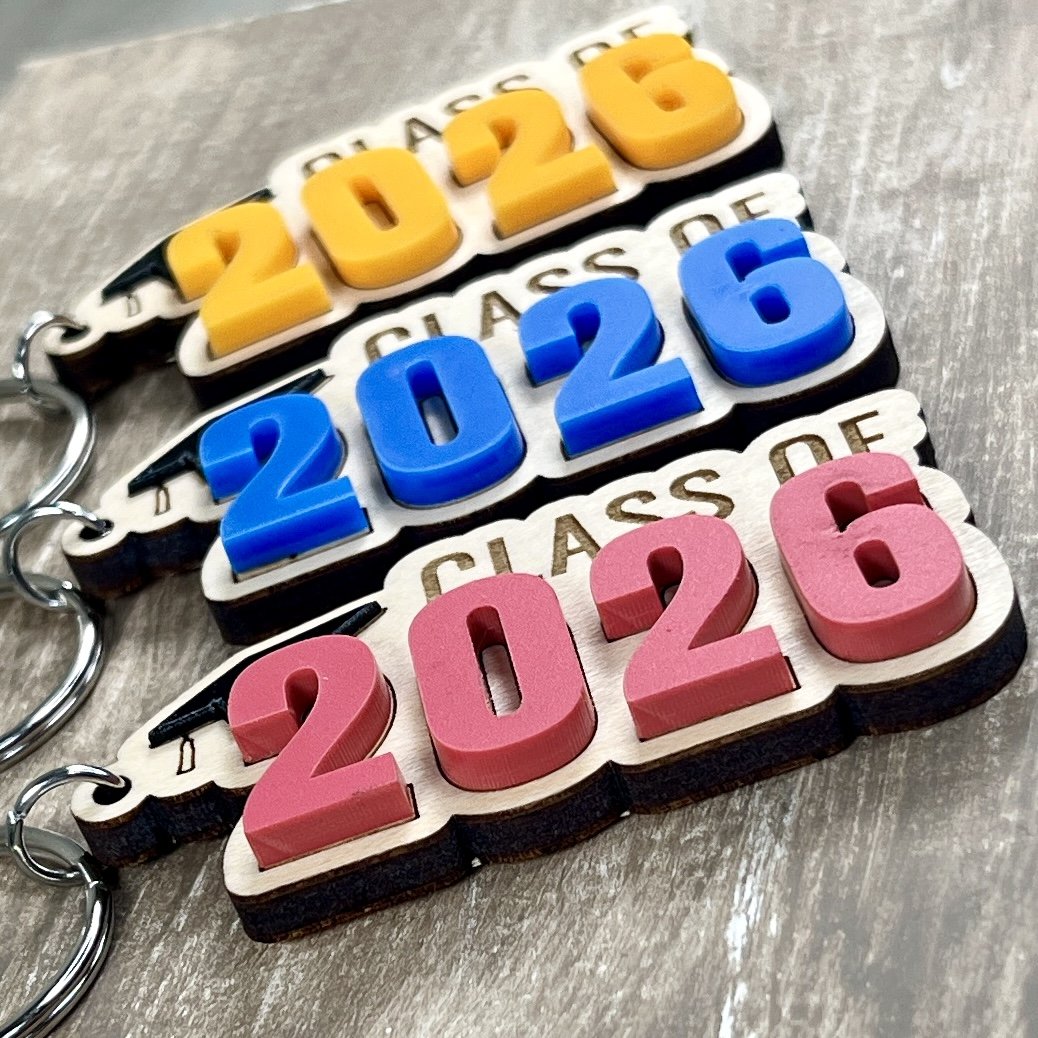 Three Class Of graduation keychains arranged side by side, each featuring a different acrylic year colour layered on maple wood.