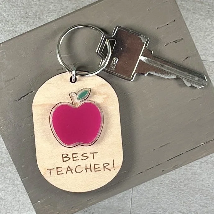 lifestyle shot of laser cut maple wood keychain featuring raised matte red acrylic apple and engraved with the phrase "BEST TEACHER!".
