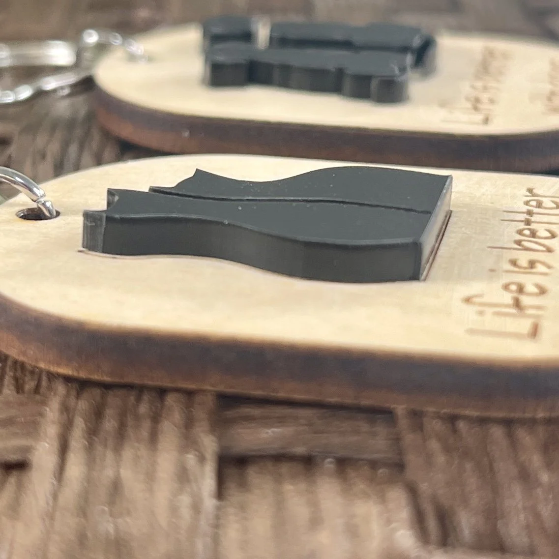 side view of laser cut maple wood keychain, displaying silhouette of two cats in raised black matte acrylic to show depth and texture of product.