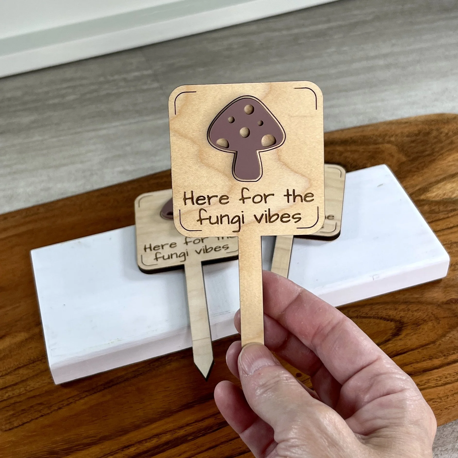 handheld maple plant stake featuring an acrylic mushroom embellishment engraved with the phrase "Here for the Fungi Vibes".
