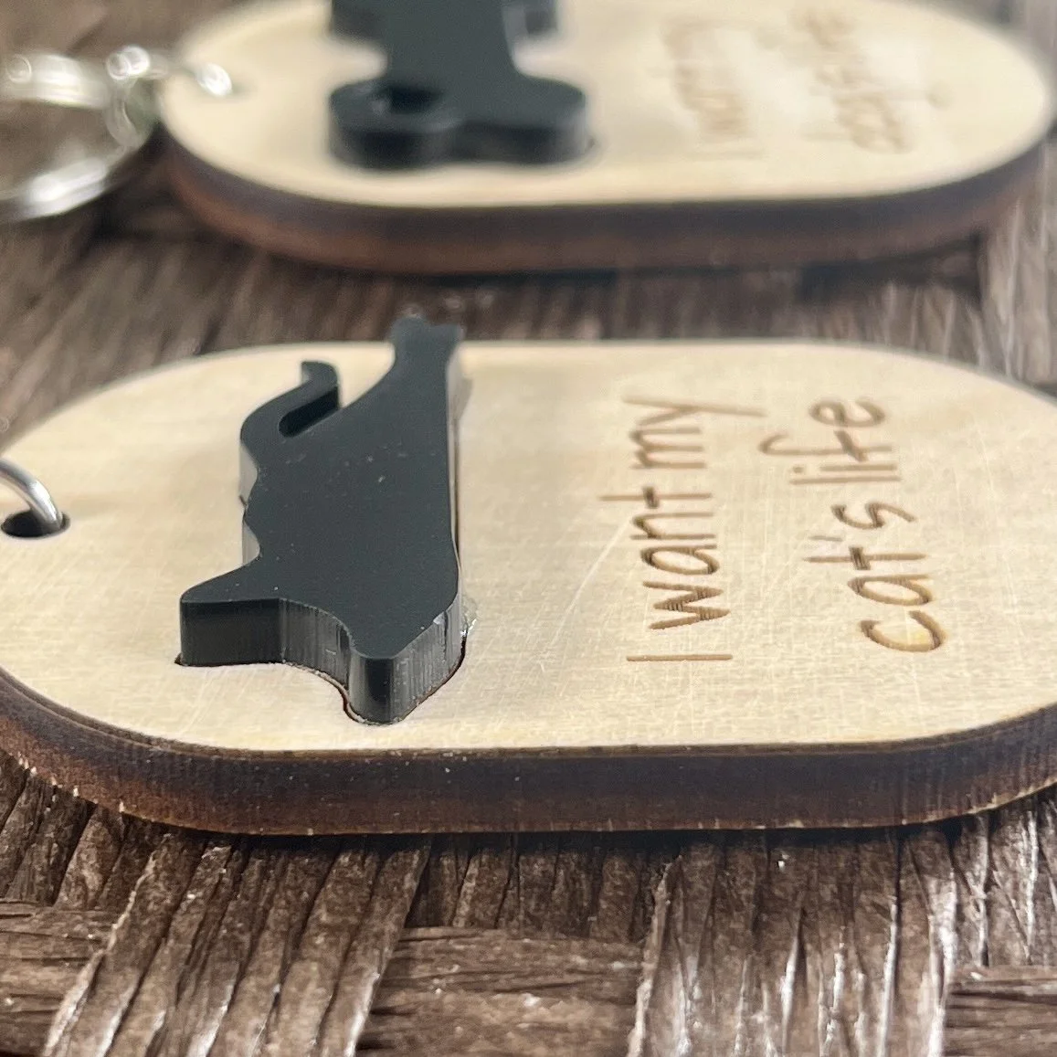 side view of laser cut maple keychain displaying silhouette of cat in raised matte black acrylic to highlight depth and texture of product.