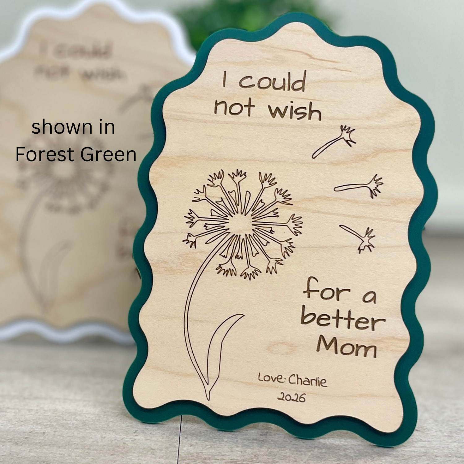 angled view of maple wood sign with green acrylic border in a wavy-edged rectangular shape, engraved with a dandelion illustration and the message "I could not wish for a better Mom."