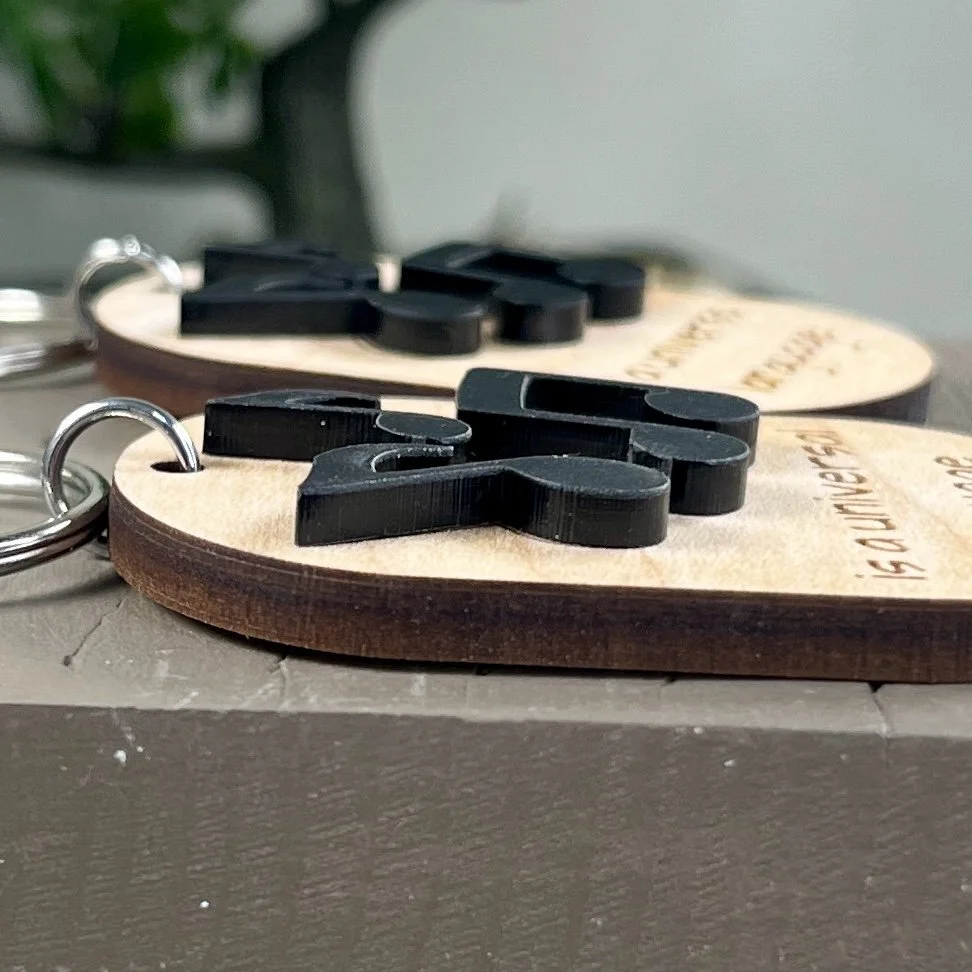 side view of laser cut maple wood keychain featuring three raised musical notes in matte black acrylic highlighting the depth and texture of the product.