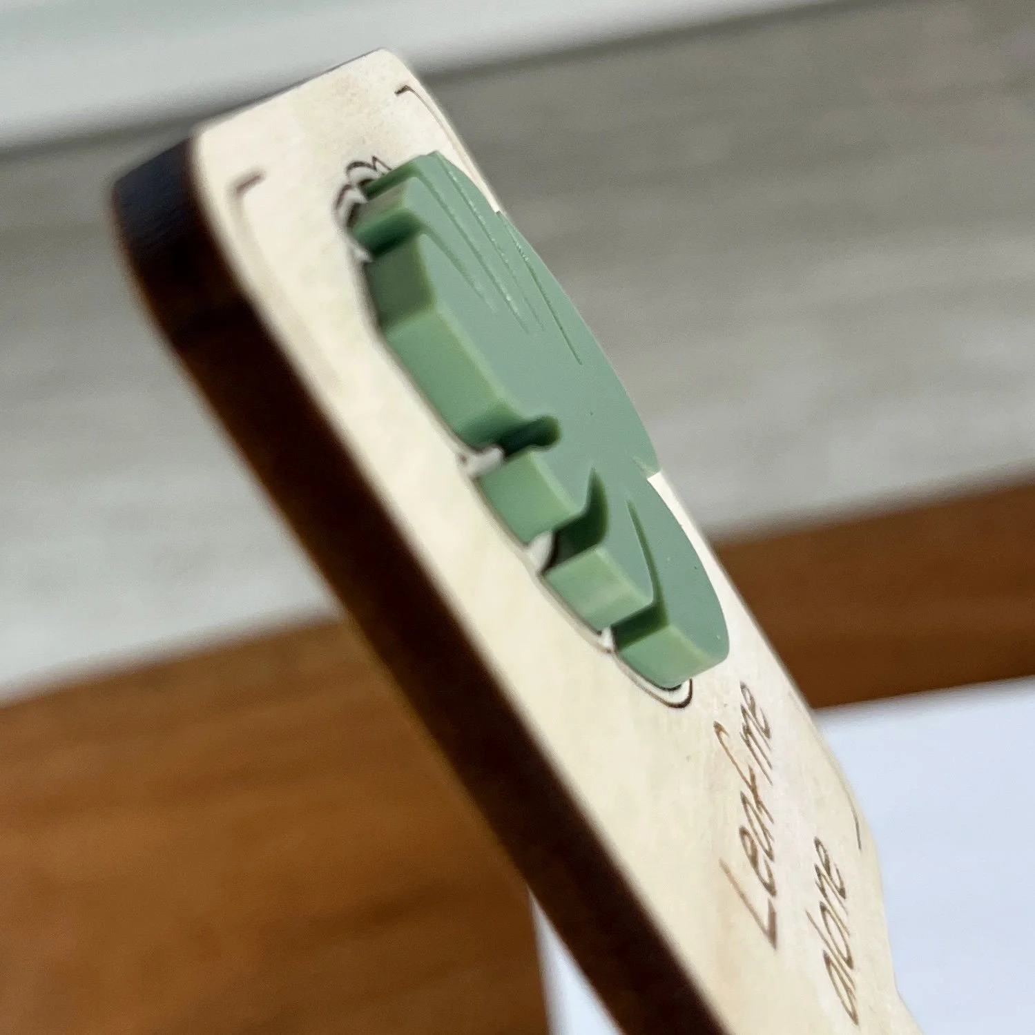 angled view maple plant stake featuring a monstera leaf embellishment engraved with the phrase "Leaf me alone".