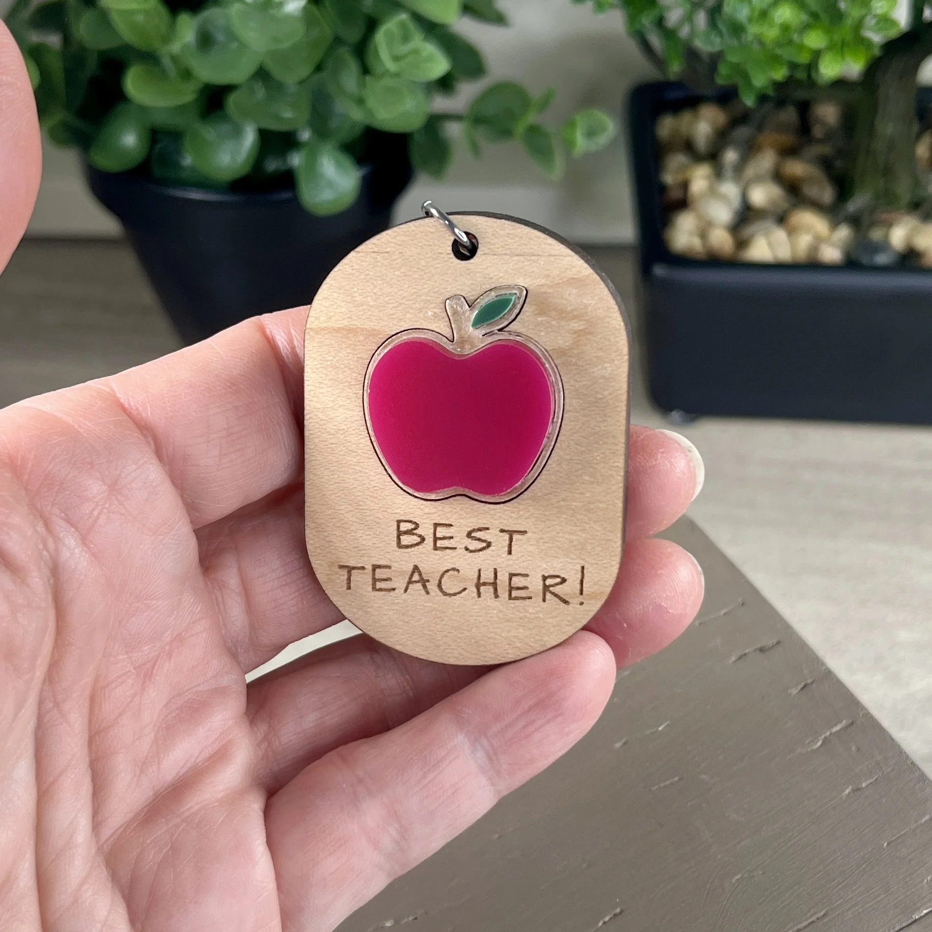 handheld laser cut maple wood keychain featuring raised matte red acrylic apple and engraved with the phrase "BEST TEACHER!".