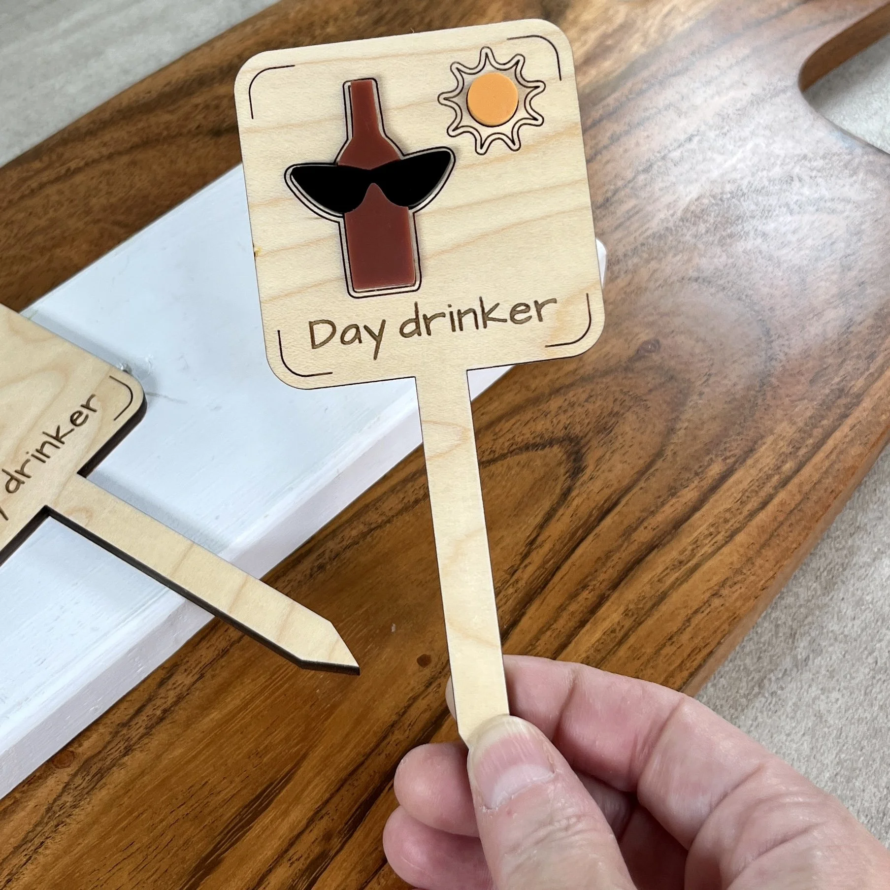 handheld maple plant stake featuring layered acrylic bottle, sunglasses and sun embellishments engraved with the phrase "Day Drinker".