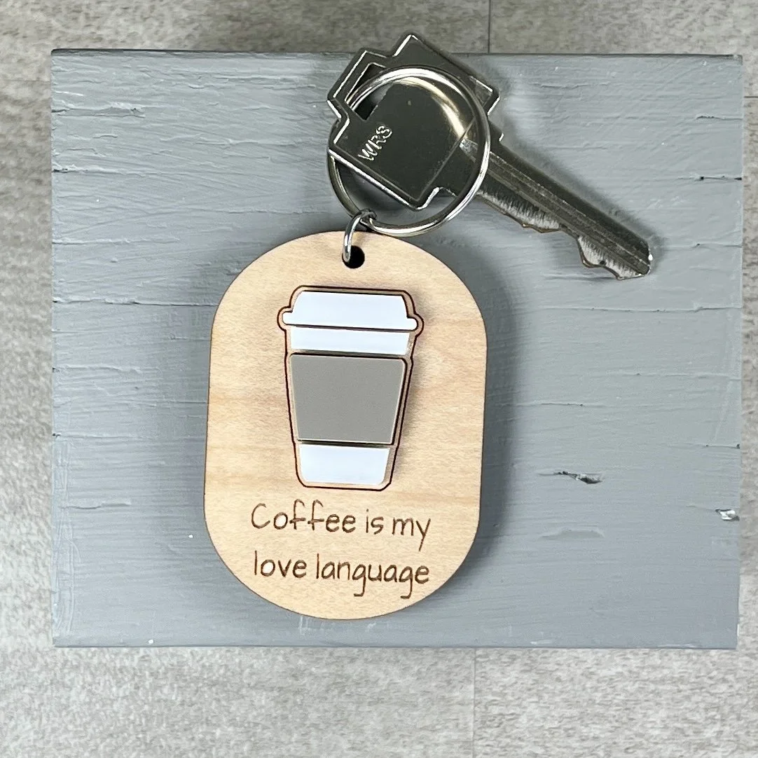 lifestyle view of laser cut maple keychain showing coffee cup graphic in raised matte white/espresso acrylic and engraved with "Coffee is my love language".