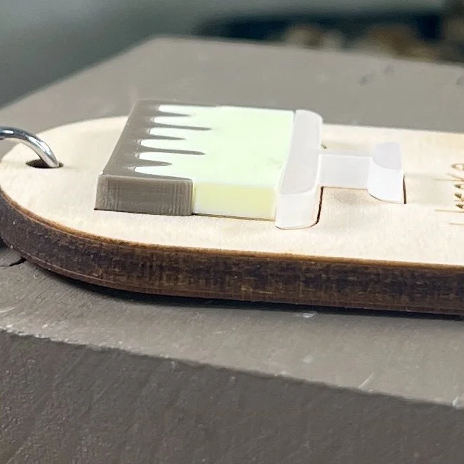 side view of laser cut maple wood keychain featuring raised matte acrylic iced layer cake on a platter highlighting the depth and texture of the product.