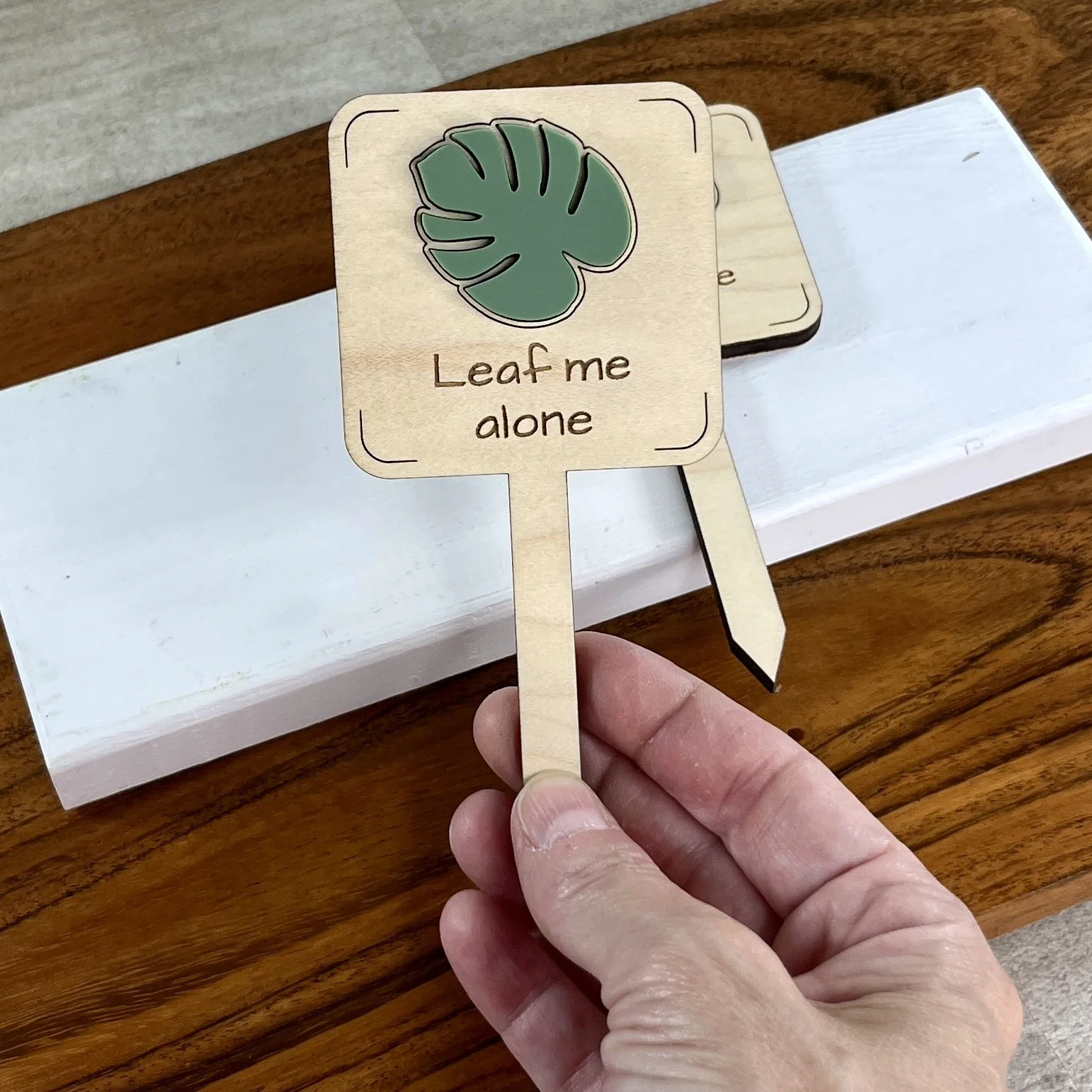 handheld maple plant stake featuring a monstera leaf embellishment engraved with the phrase "Leaf me alone".
