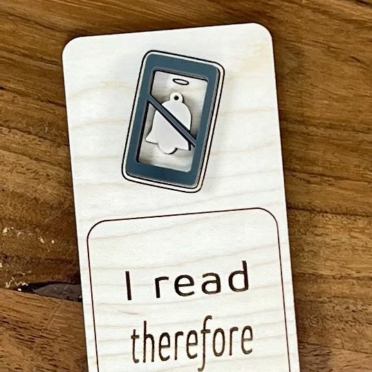 close up maple bookmark featuring a blue acrylic do not disturb symbol embellishment engraved with the phrase "I read therefore I ignore people".