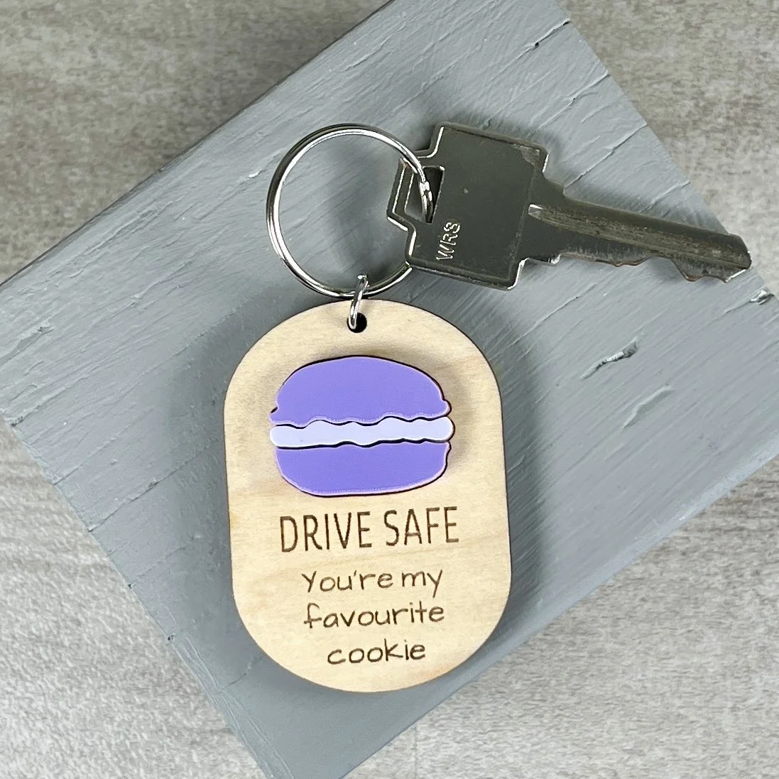 lifestyle shot of laser cut maple wood keychain with macaron cookie in matte orchid/white acrylic and the engraved phrase "DRIVE SAFE You're my favourite cookie".