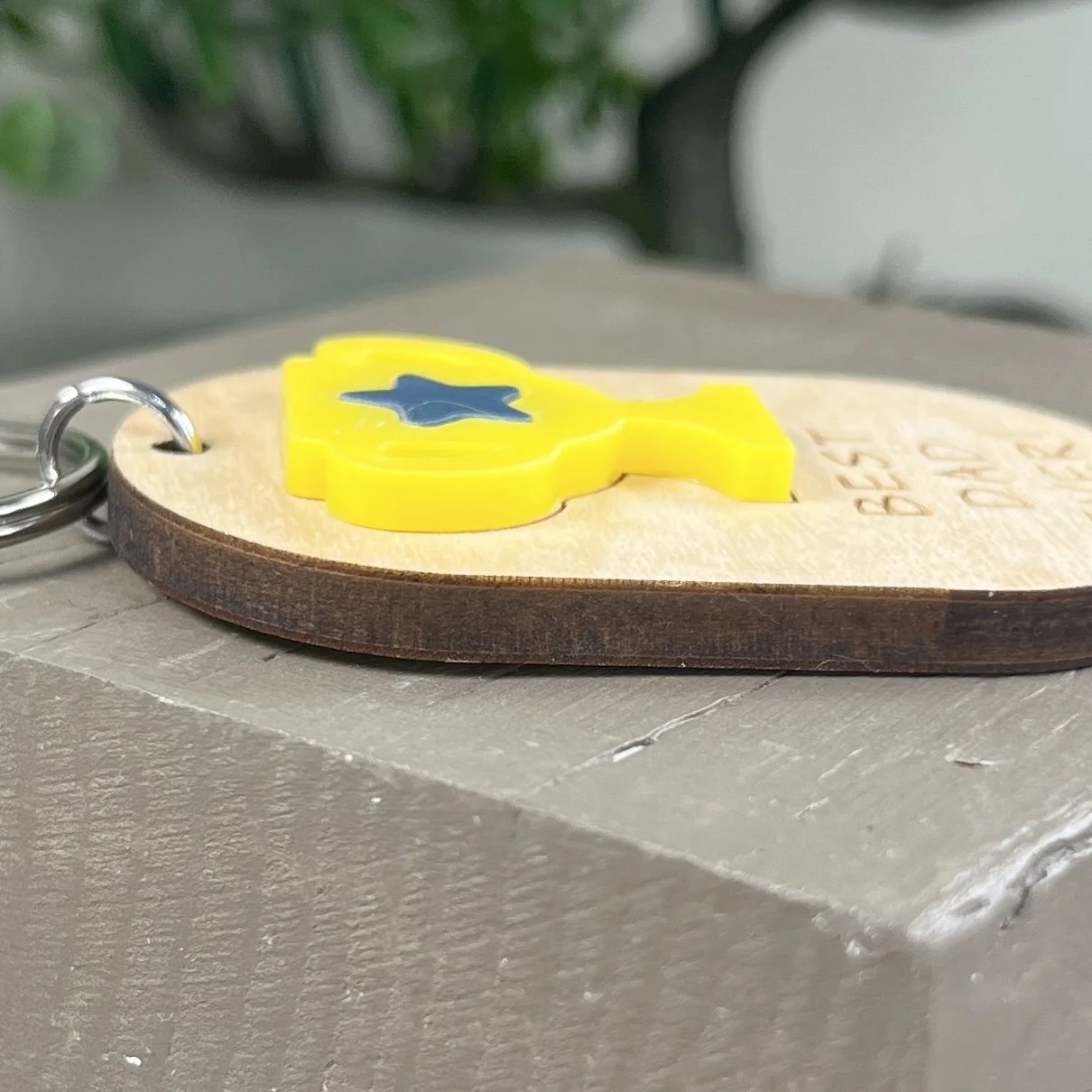 side view of laser cut maple wood keychain featuring matte bumblebee yellow acrylic trophy decorated with a navy blue acrylic star to highlight the depth and texture of the product.