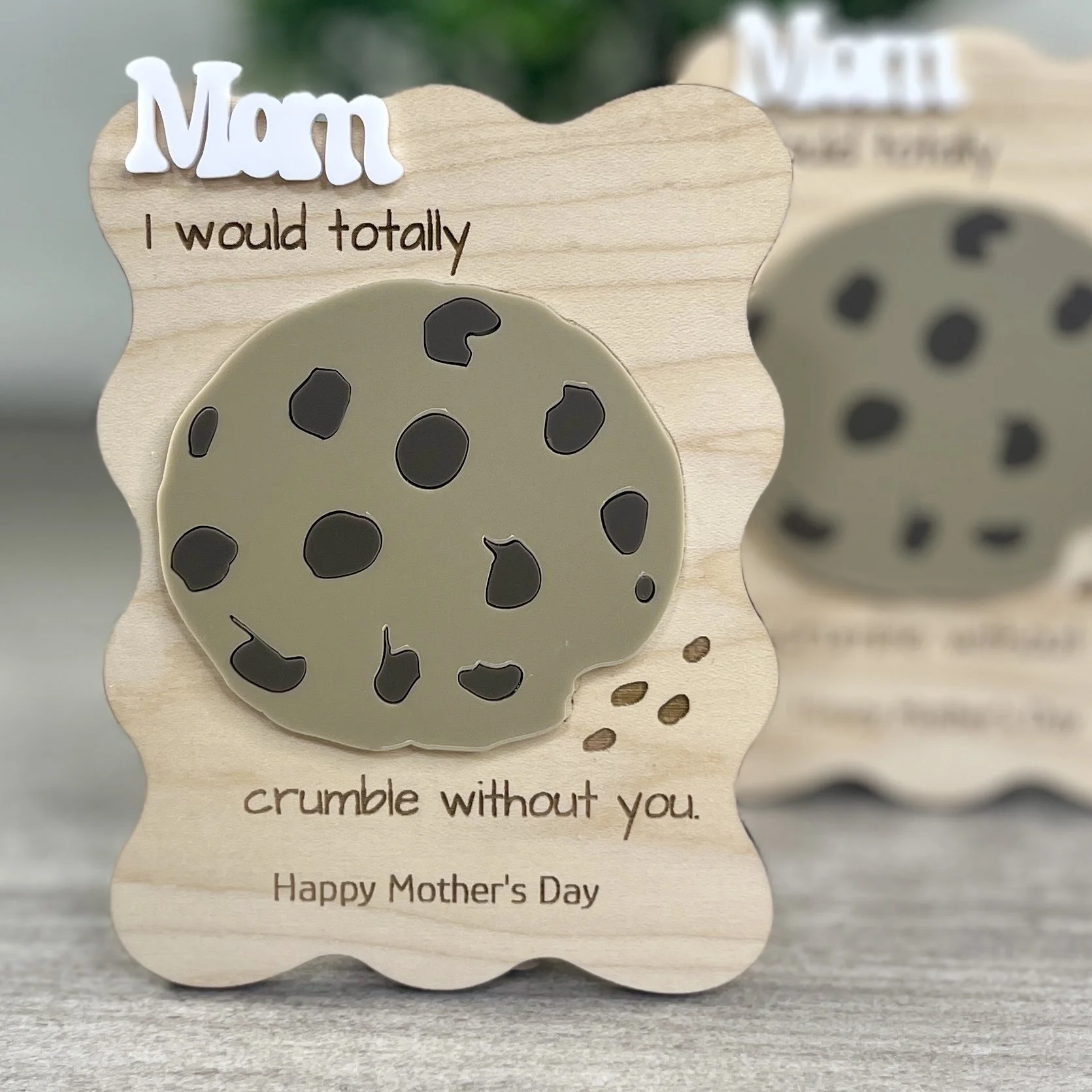 two front-facing wavy-edged maple magnets featuring the word Mom in raised white acrylic, a chocolate chip cookie in acrylic and engraved with the phrase "I would totally crumble without you".
