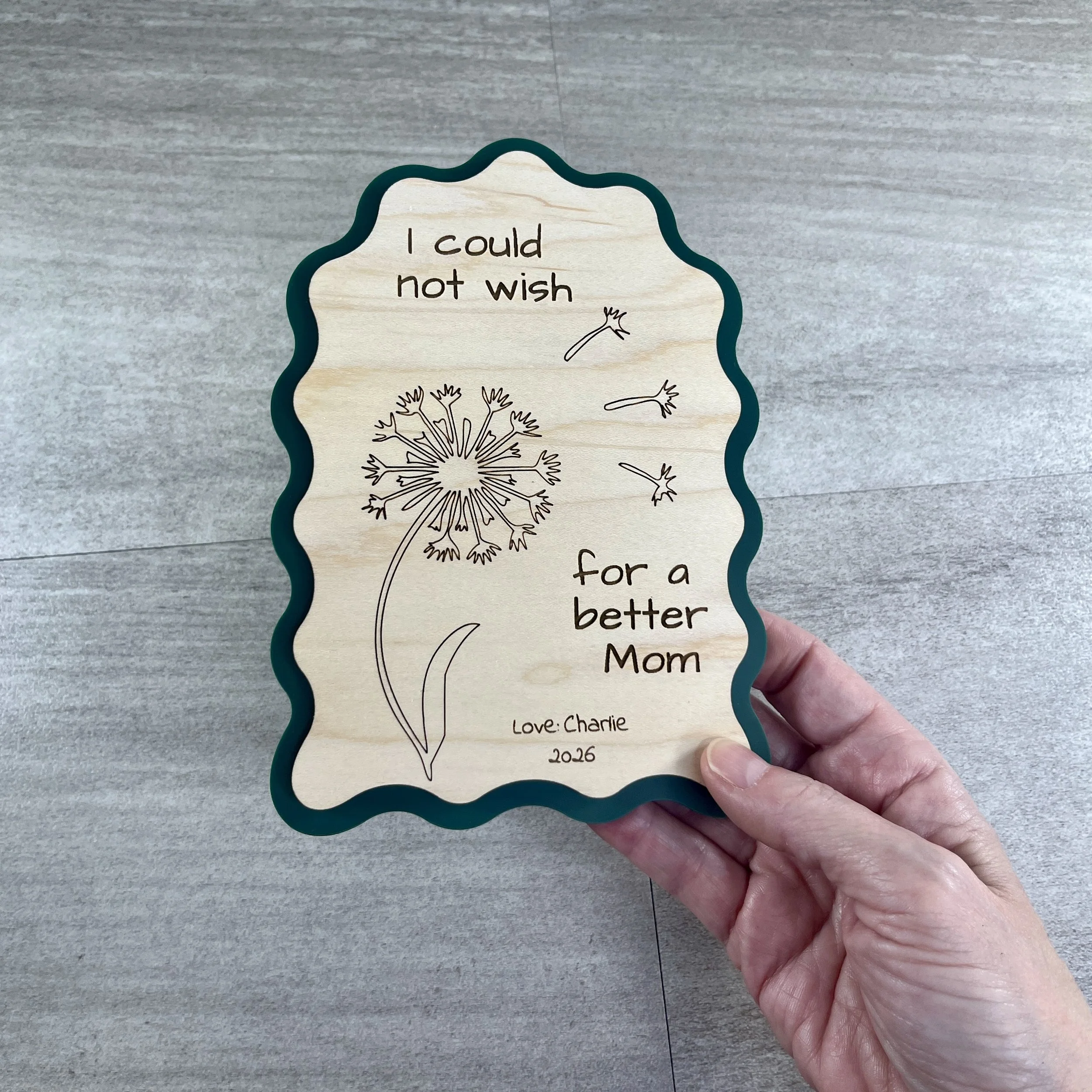 handheld maple wood sign with green acrylic border in a wavy-edged rectangular shape, engraved with a dandelion illustration and the message "I could not wish for a better Mom."