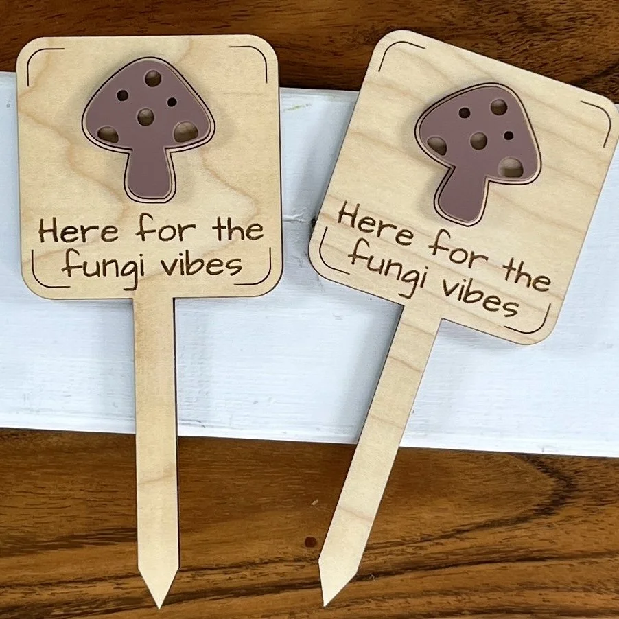 flat lay maple plant stake featuring an acrylic mushroom embellishment engraved with the phrase "Here for the Fungi Vibes".