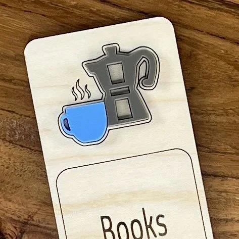 close up maple bookmark featuring blue acrylic coffee cup and stovetop coffee pot embellishment engraved with the phrase "Books and Coffee".