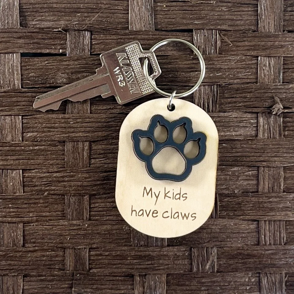 handheld shot of laser cut wood keychain with matte black claw and engraved saying "My kids have claws".