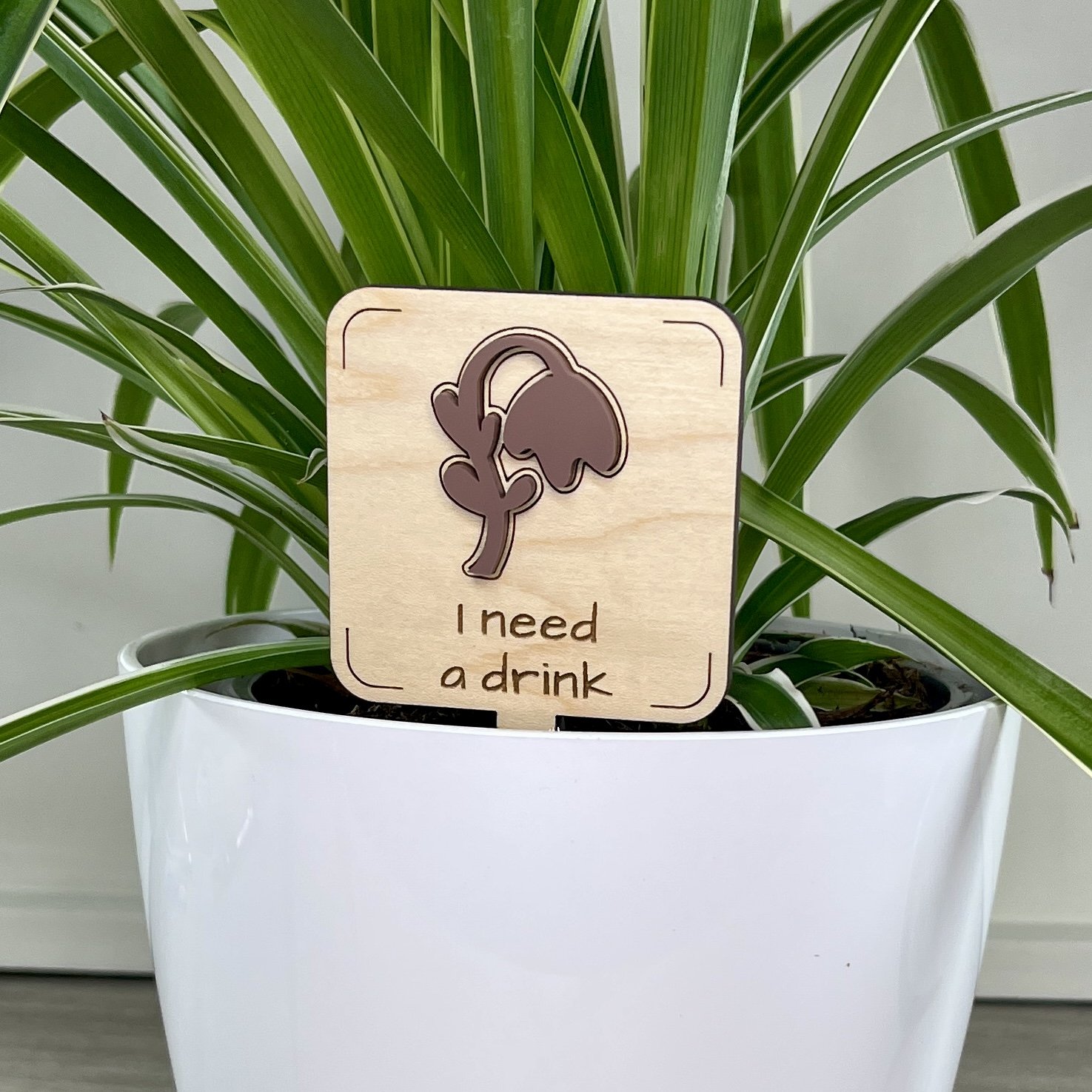 maple plant stake displayed in a potted houseplant featuring a droopy plant embellishment engraved with the phrase "I need a drink".