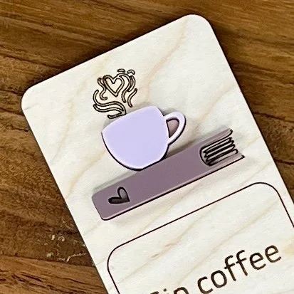close up maple bookmark featuring an ash rose coffee cup and mauve book embellishment engraved with the phrase "Sip coffee Read books Stay cozy".