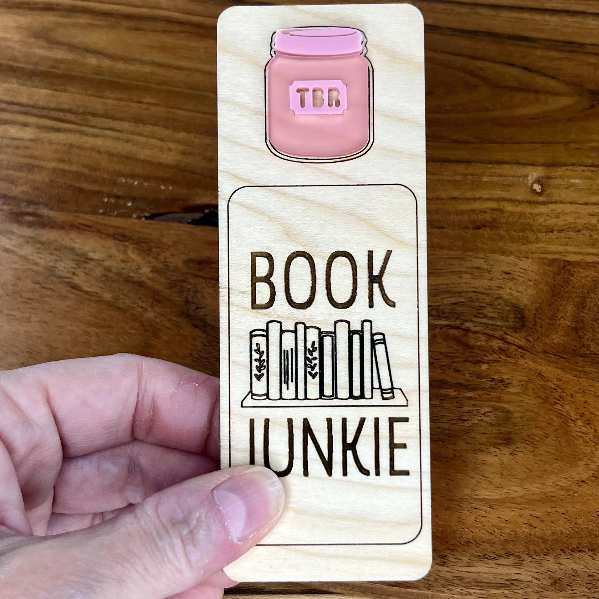 handheld maple bookmark showing pink acrylic TBR jar embellishment and engraved phrase "Book Junkie".