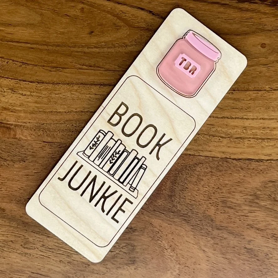 flat lay maple bookmark featuring pink acrylic TBR jar embellishment engraved with the phrase "Book Junkie".