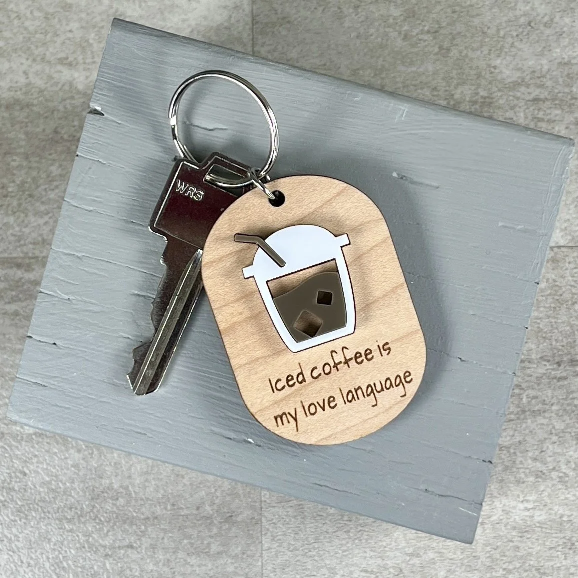 lifestyle shot of laser cut maple keychain showing iced coffee graphic in raised matte white/espresso acrylic and engraved with "Iced coffee is my love language".
