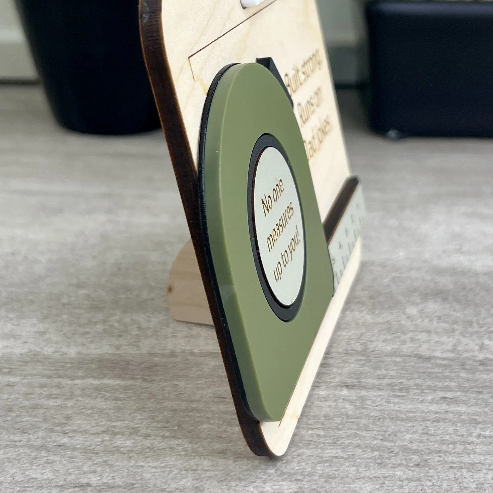 Side view of laser cut maple magnet with raised olive acrylic tape measure design highlighting depth and texture of product.