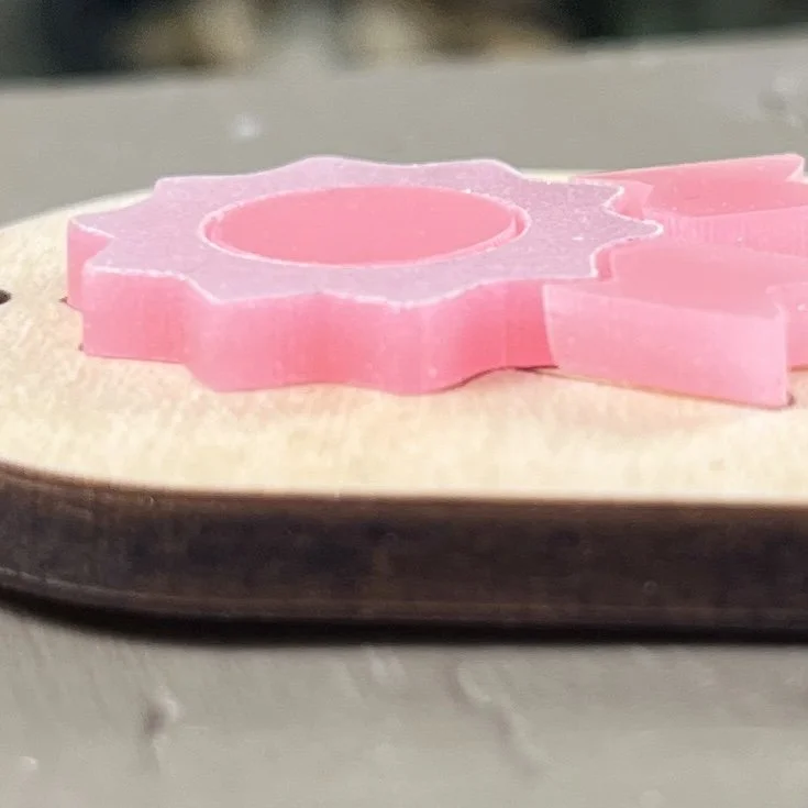 side view of laser cut maple wood keychain featuring raised glimmering/gloss pink acrylic ribbon highlighting the depth and texture of the product.
