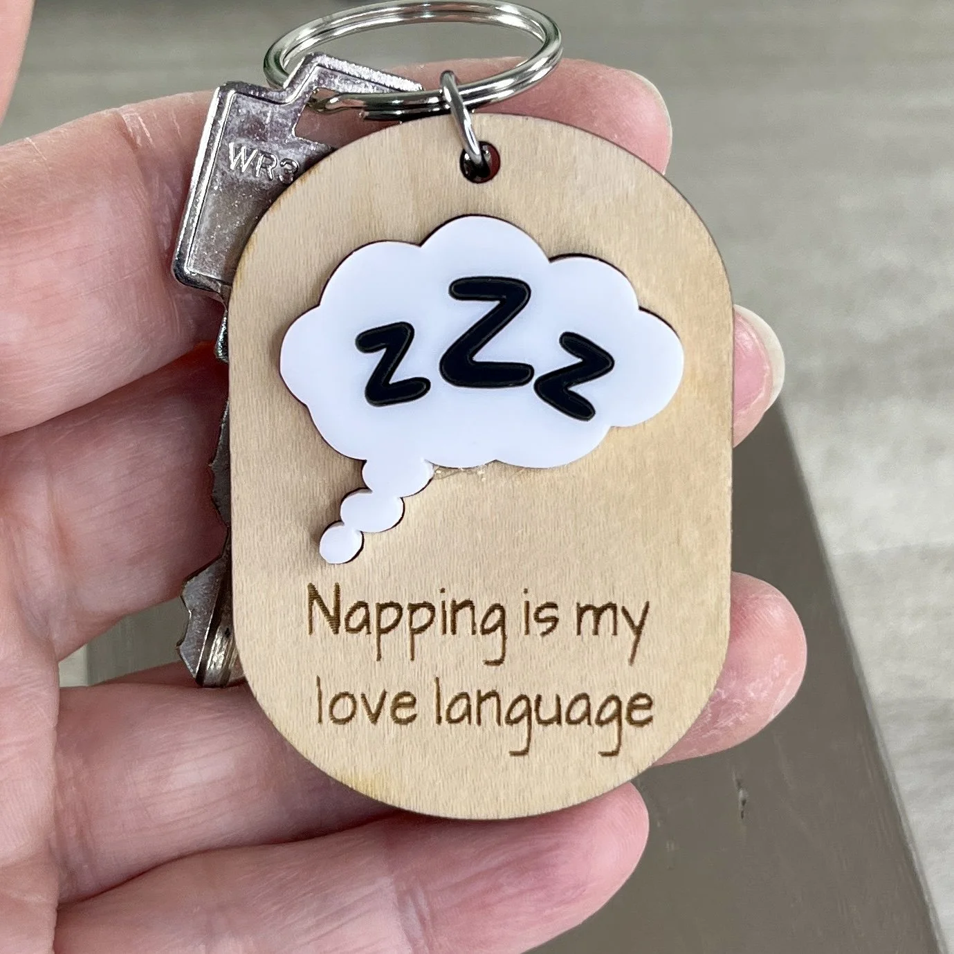 handheld view of laser cut maple keychain with ZZZ in thought bubble in raised white/black matte acrylic and engraved with "Napping is my love language".