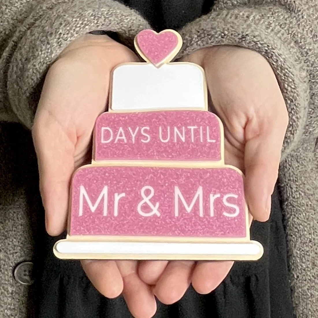 Laser cut wood magnets in the shape of tiered wedding cake, featuring acrylic elements, held in hand for scale.