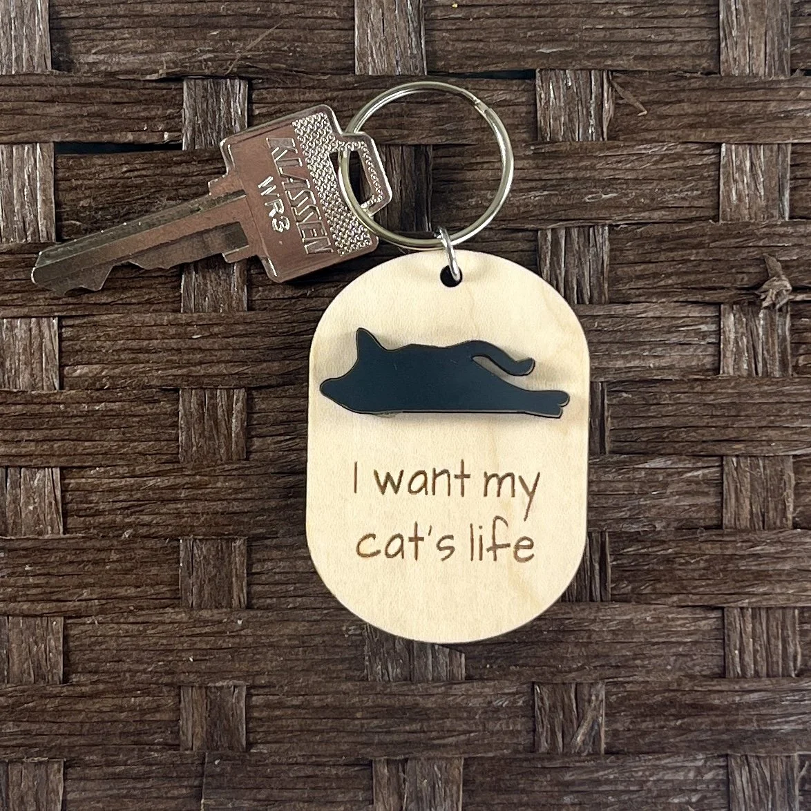 lifestyle image of laser cut maple keychain with cat silhouette in matte black acrylic and engraved with the saying "I want my cat's life".