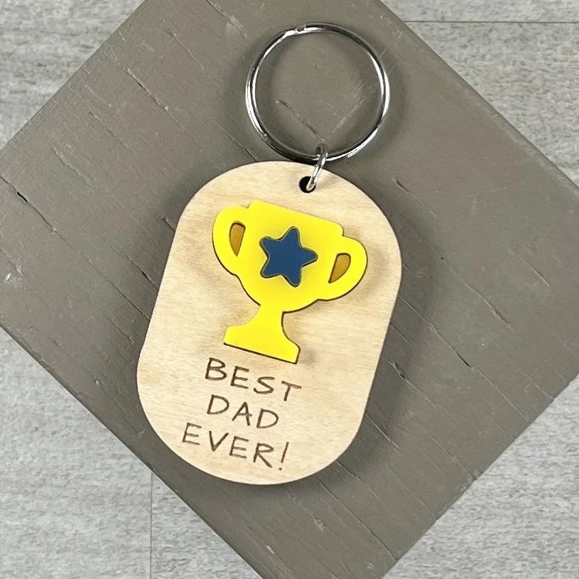 flat lay of laser cut maple wood keychain featuring matte bumblebee yellow acrylic trophy decorated with a navy blue acrylic star and the engraved phrase "BEST DAD EVER!"