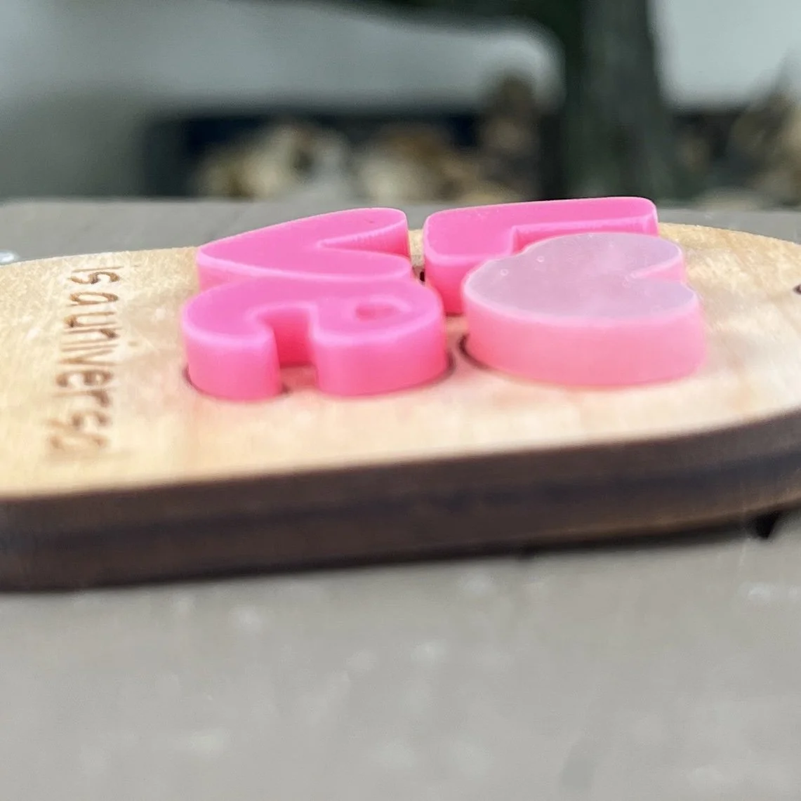 side shot of laser cut maple wood keychain featuring layered pink acrylic letters spelling "Love" with heart details highlighting the depth and texture of the product.