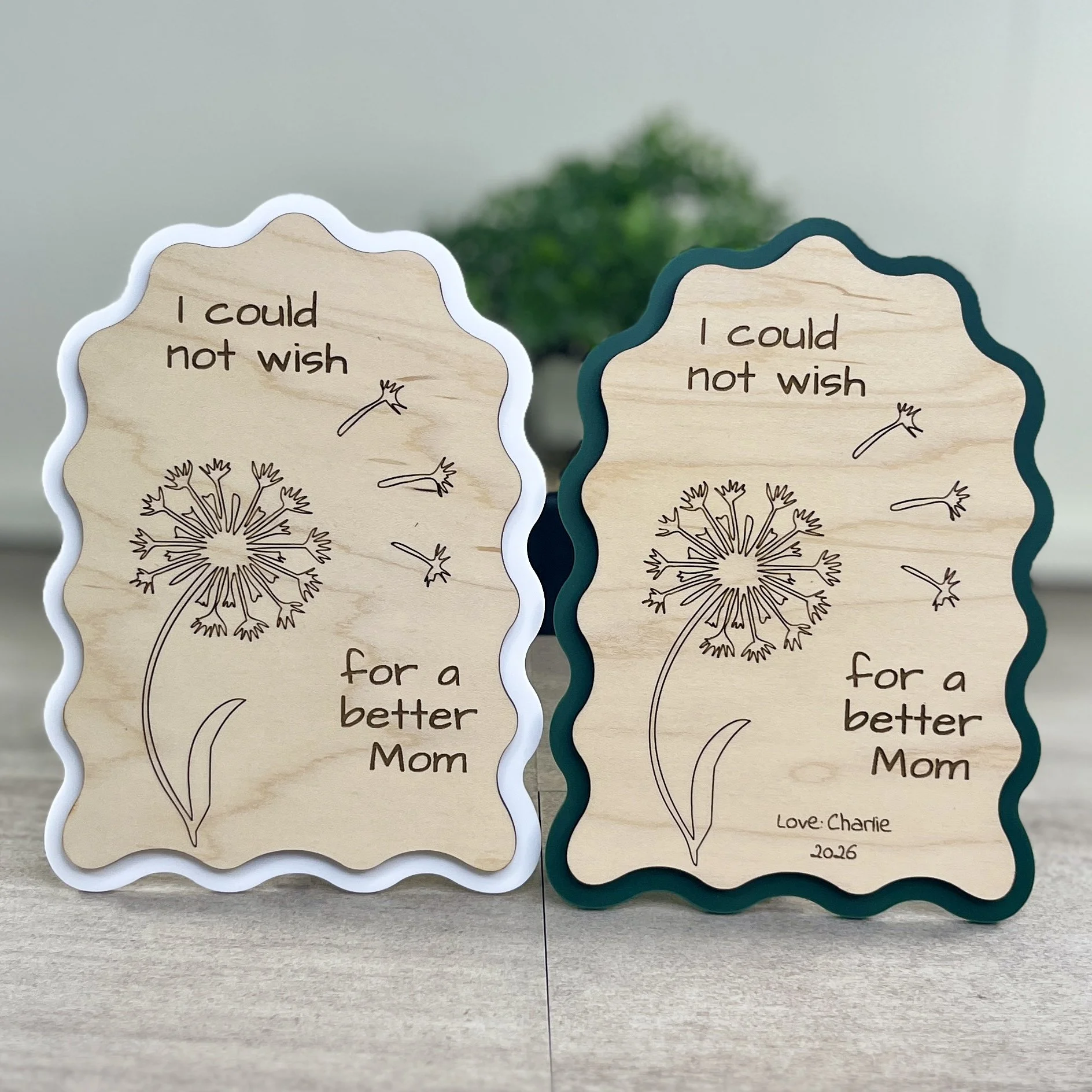 front view of two maple wood signs (one with white acrylic border/the other green) in a wavy-edged rectangular shape, engraved with a dandelion and the message "I could not wish for a better Mom."