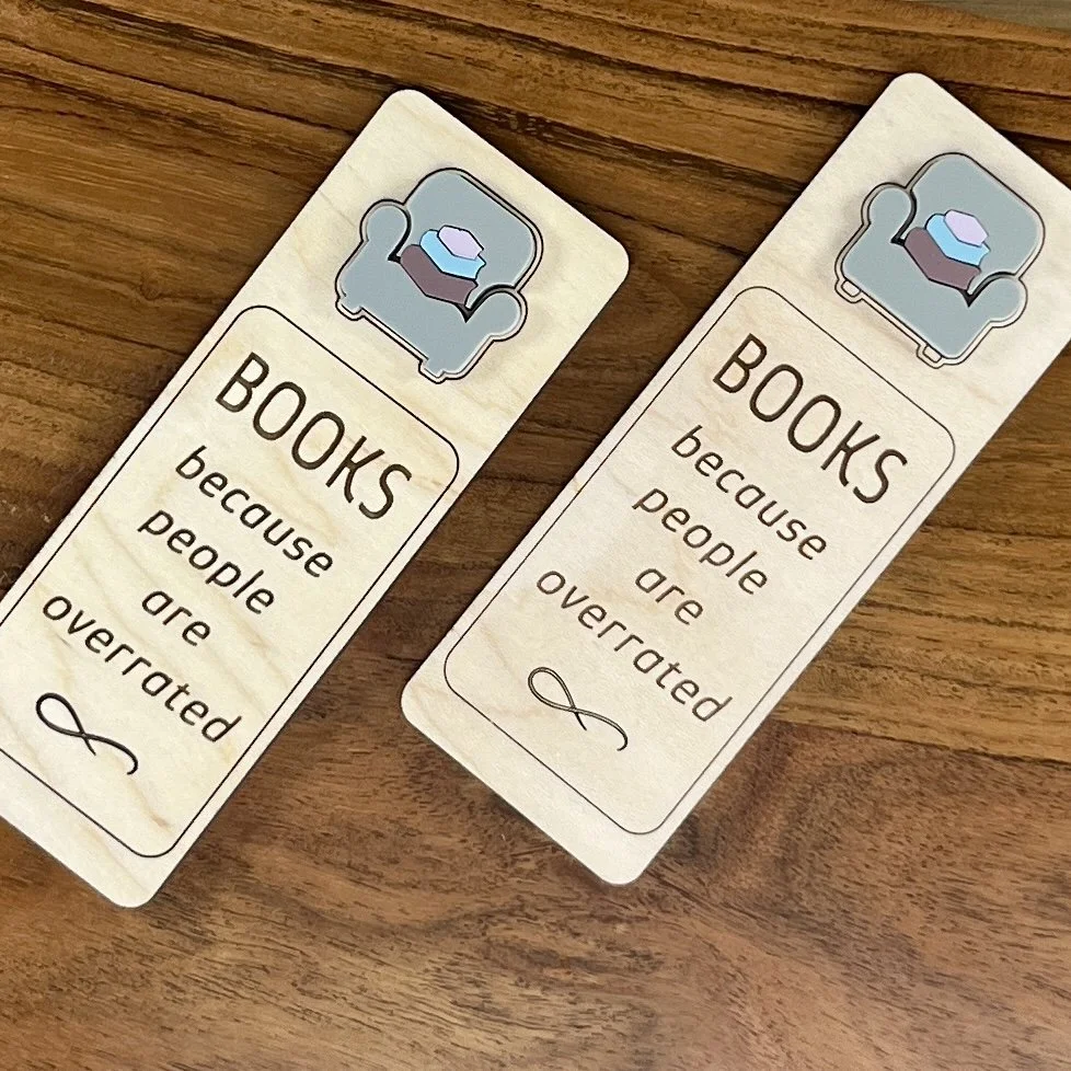 flat lay maple bookmark featuring blue acrylic reading chair and stack of books embellishment engraved with the phrase "Books Because People Are Overrated".
