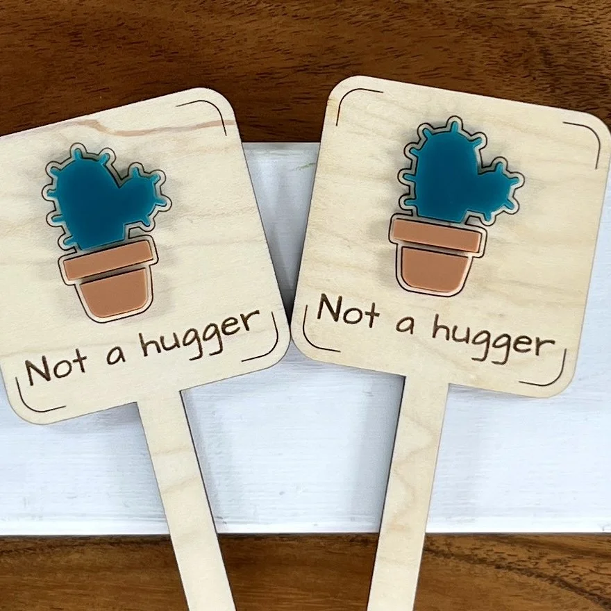 flat lay maple plant stake featuring a prickly succulent embellishment engraved with the phrase "Not a hugger".
