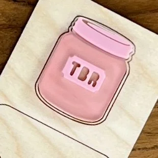 close up maple bookmark showing engraved phrase "Book Junkie" and layered pink acrylic TBR jar embellishment.