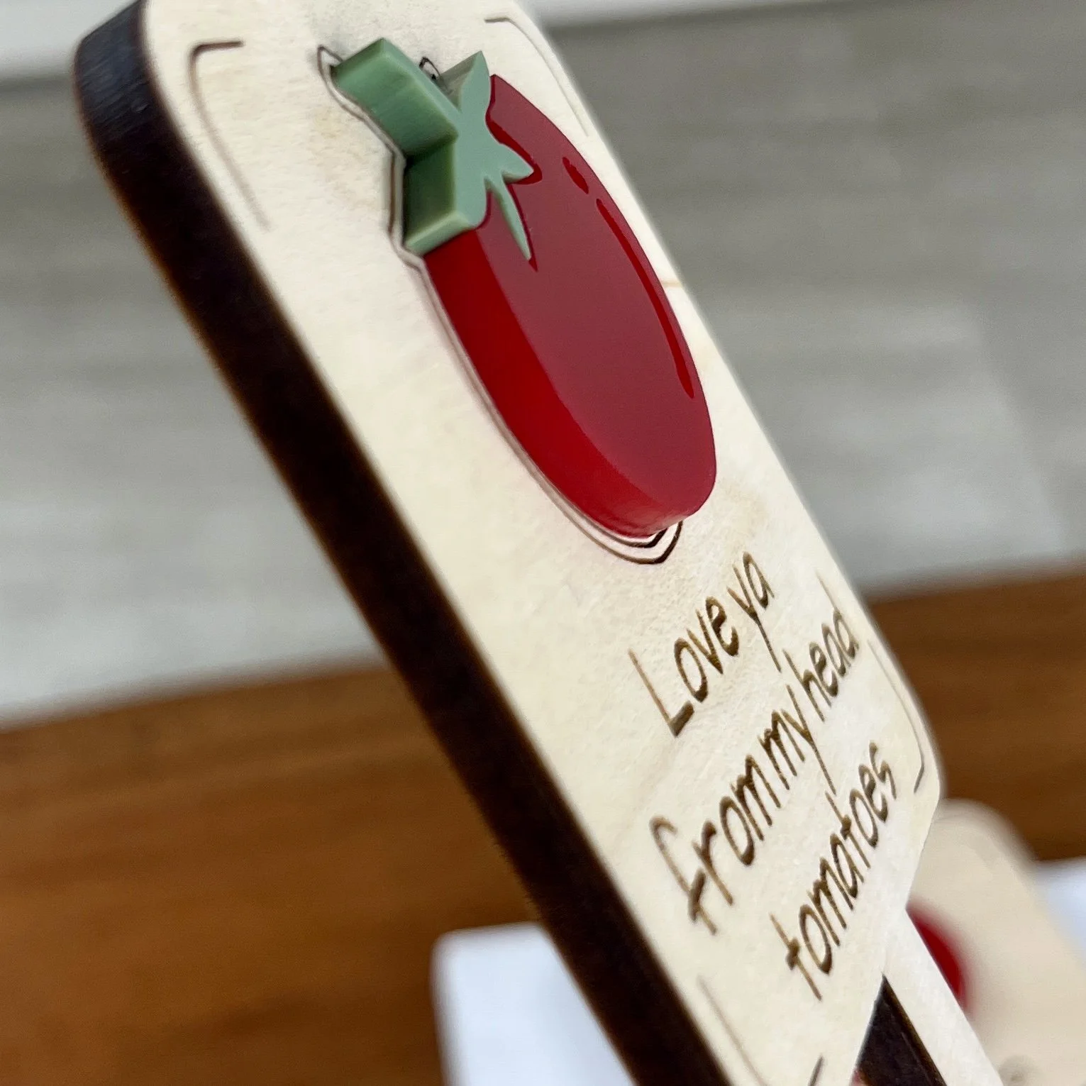 angled view maple plant stake featuring a plump red tomato embellishment engraved with the phrase "Love ya from my head tomatoes".