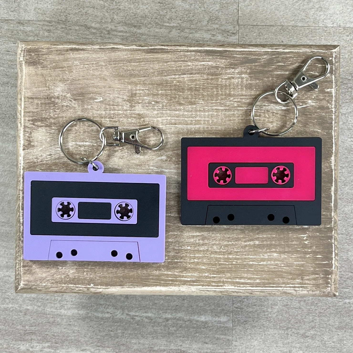 Retro cassette tape-shaped acrylic backpack tags in purple and pink, available with personalized names.
