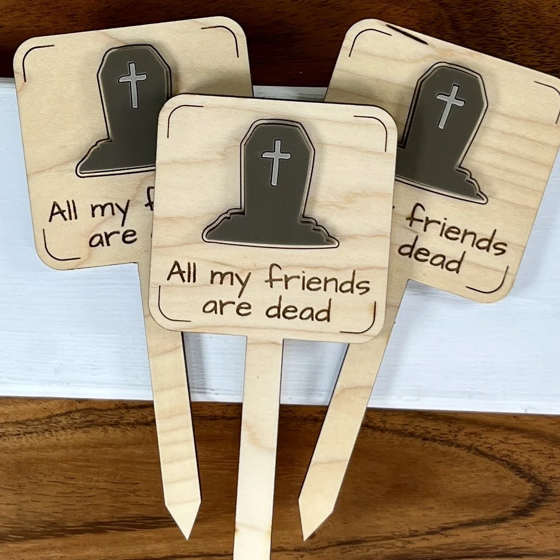 flat lay maple plant stake featuring an acrylic espresso tombstone embellishment engraved with the phrase "All my friends are dead".