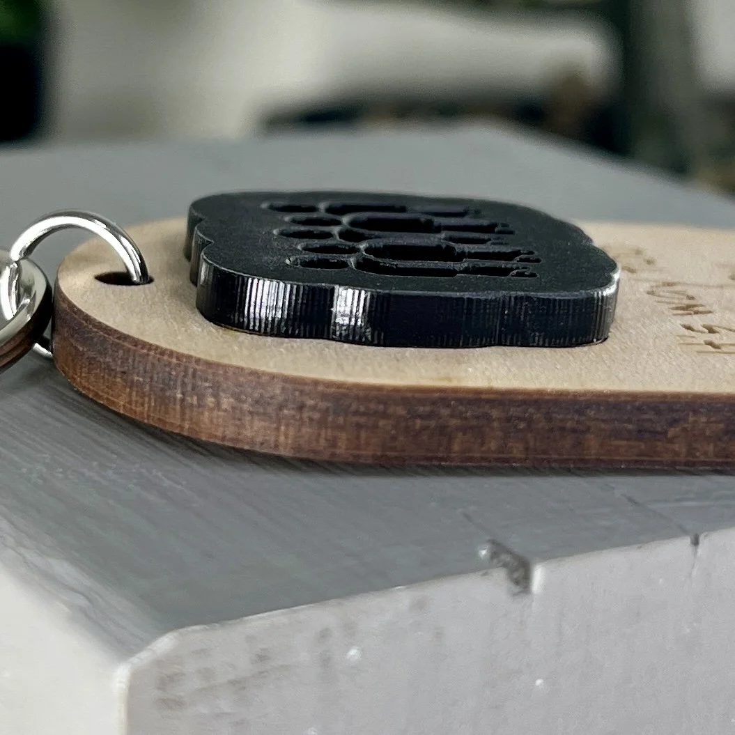 side view of laser cut maple wood keychain with silhouette of group of people in matte black acrylic highlighting the depth and texture of the product.