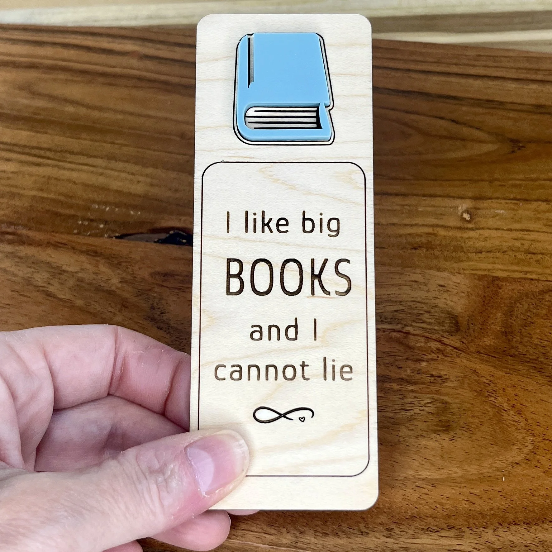 handheld maple bookmark featuring an acrylic book engraved with the phrase "I like big books and I cannot lie”.