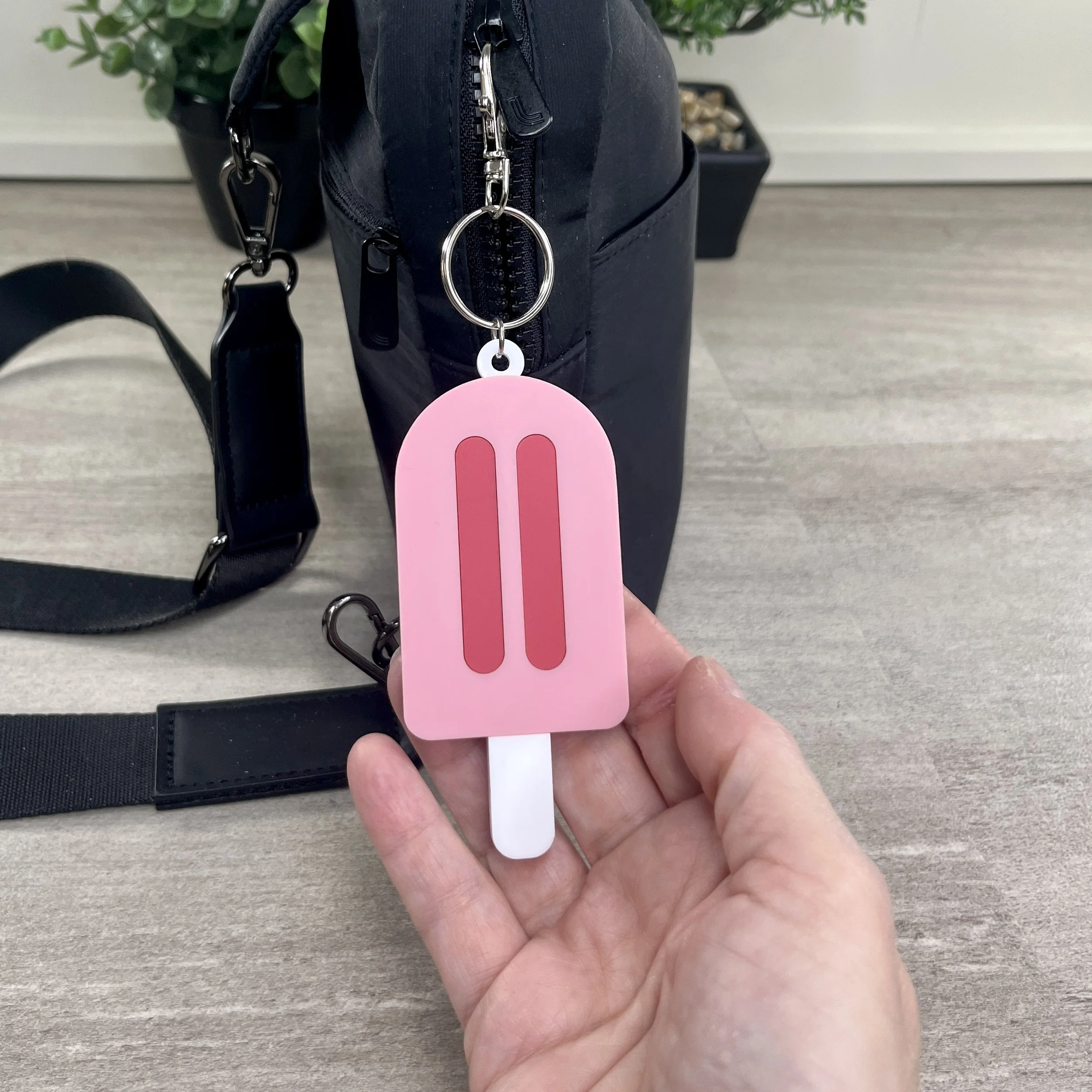 Popsicle-shaped pink acrylic backpack tag held in hand to show scale.