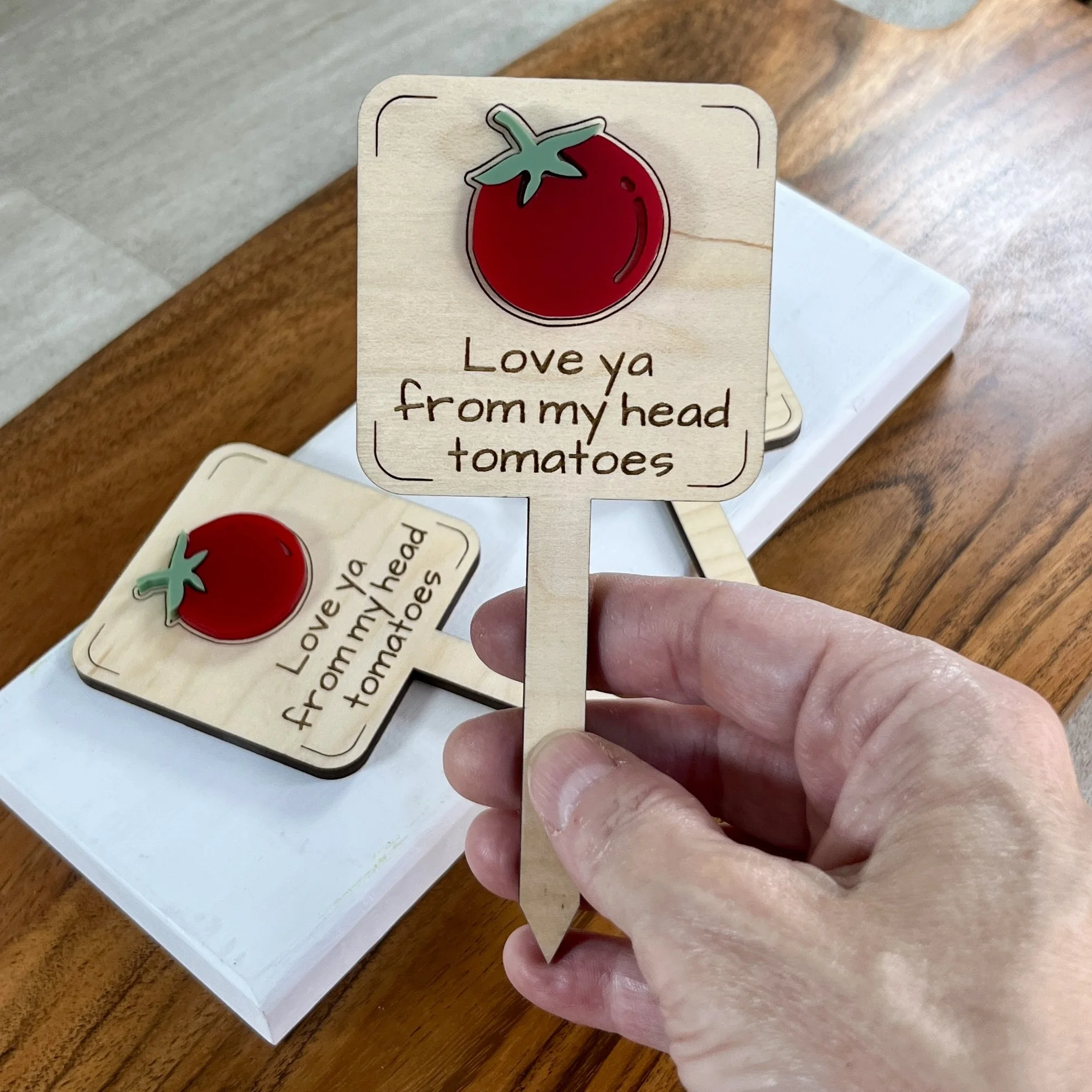 handheld maple plant stake featuring a plump red tomato embellishment engraved with the phrase "Love ya from my head tomatoes".